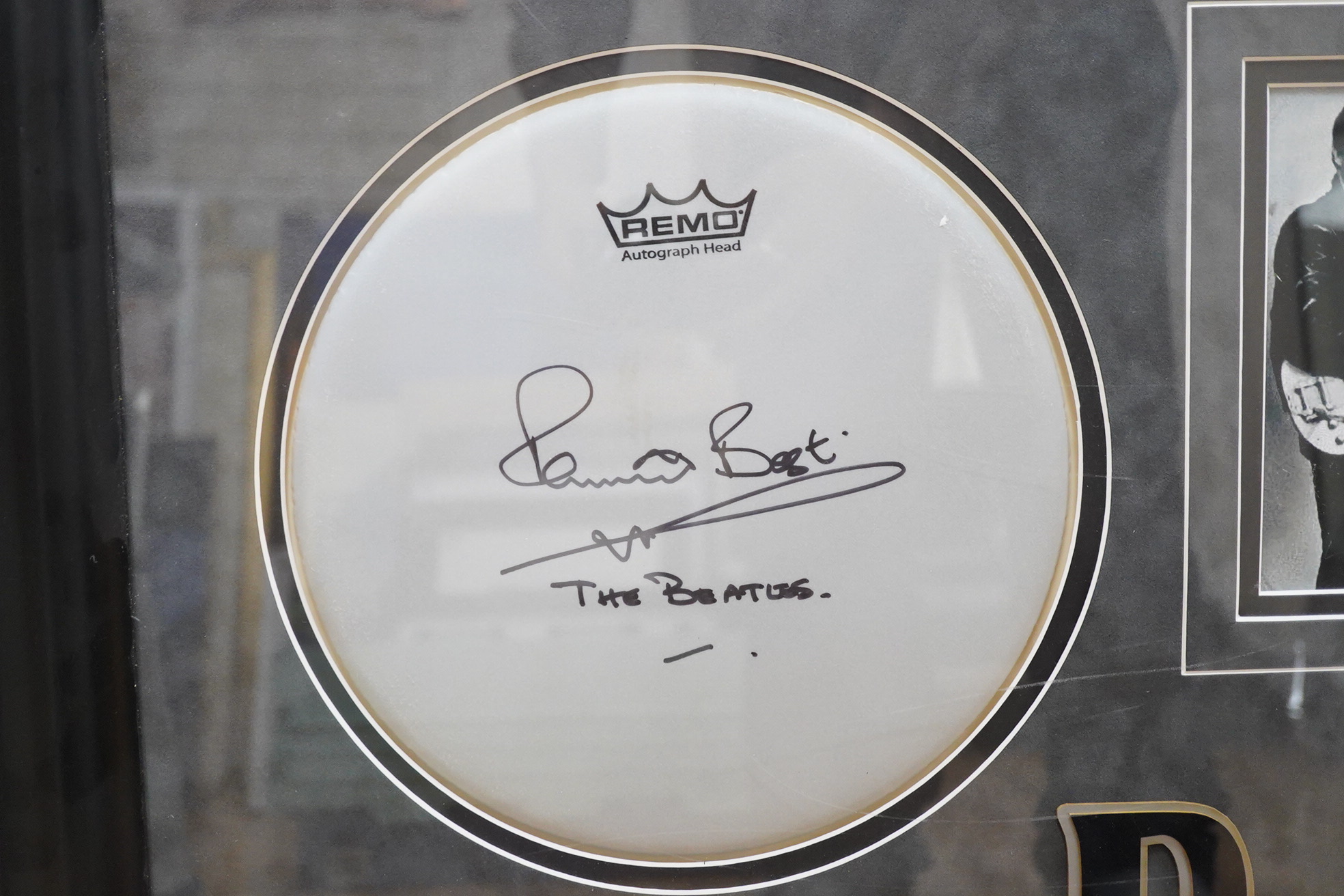 A mounted and framed Remo drum skin, signed by Pete Best, framed alongside a photograph of The Beatles including Best, with title and information panel below, oval dimensions of frame 62 x 81cm